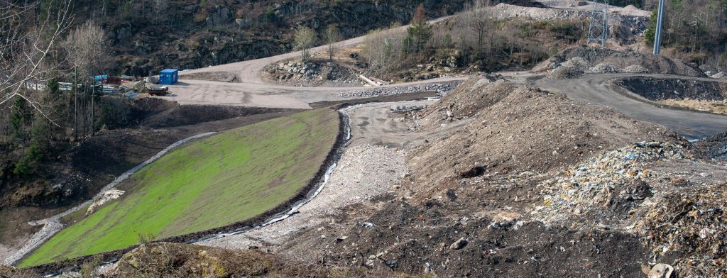 Grønn tilsådd skråning og på åpent avfallsdeponi med skog i bakgrunnen