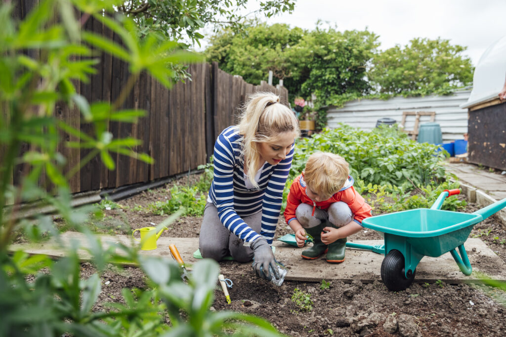 Ung dame og liten gutt sittende på huk i hagen og krafser i jorden
