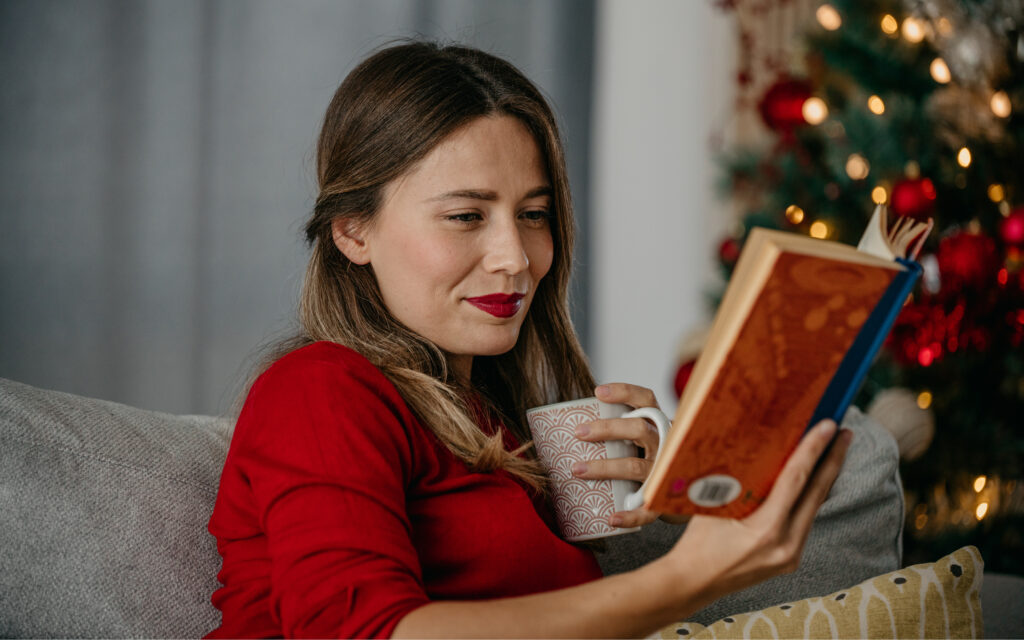 Dame som sitter og koser seg med en god bok mens hun drikker kaffe.