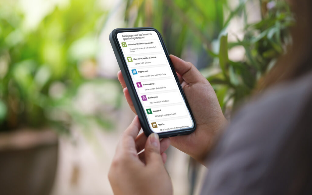 Hånd som holder mobiltelefon som viser nye nasjonale sorteringsmerker i bruk på Avfalls Sørs nettsider.