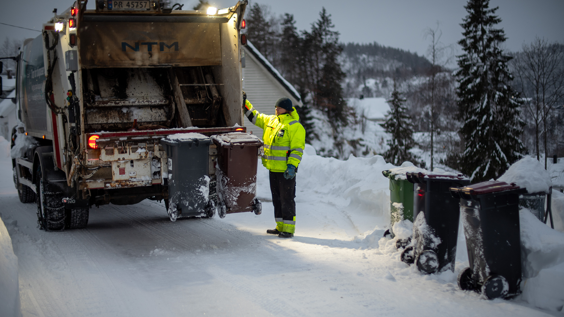 Renovasjonsbil og renovatør som henter dunker om vinteren etter stort snøfall.