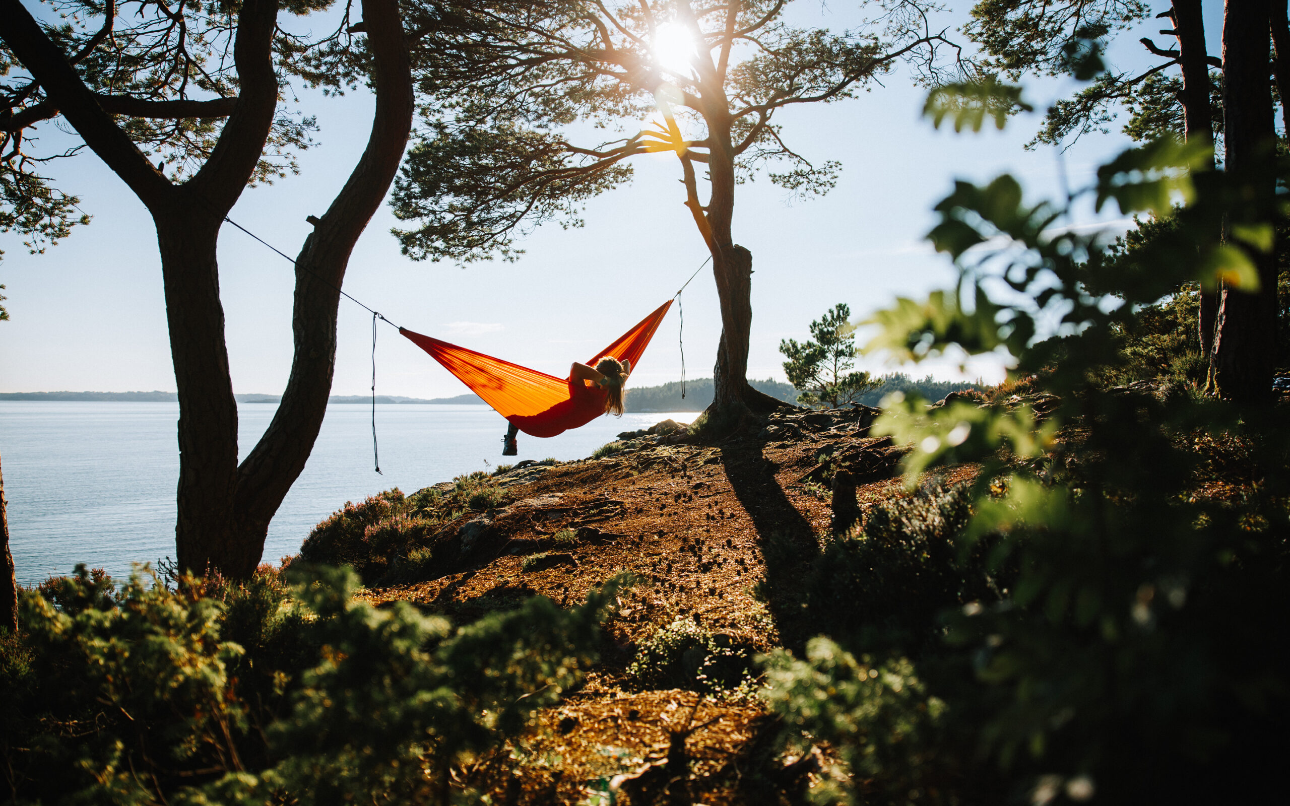 Dame som ligger og slapper av i hengekøye ved sjøen på sommeren.