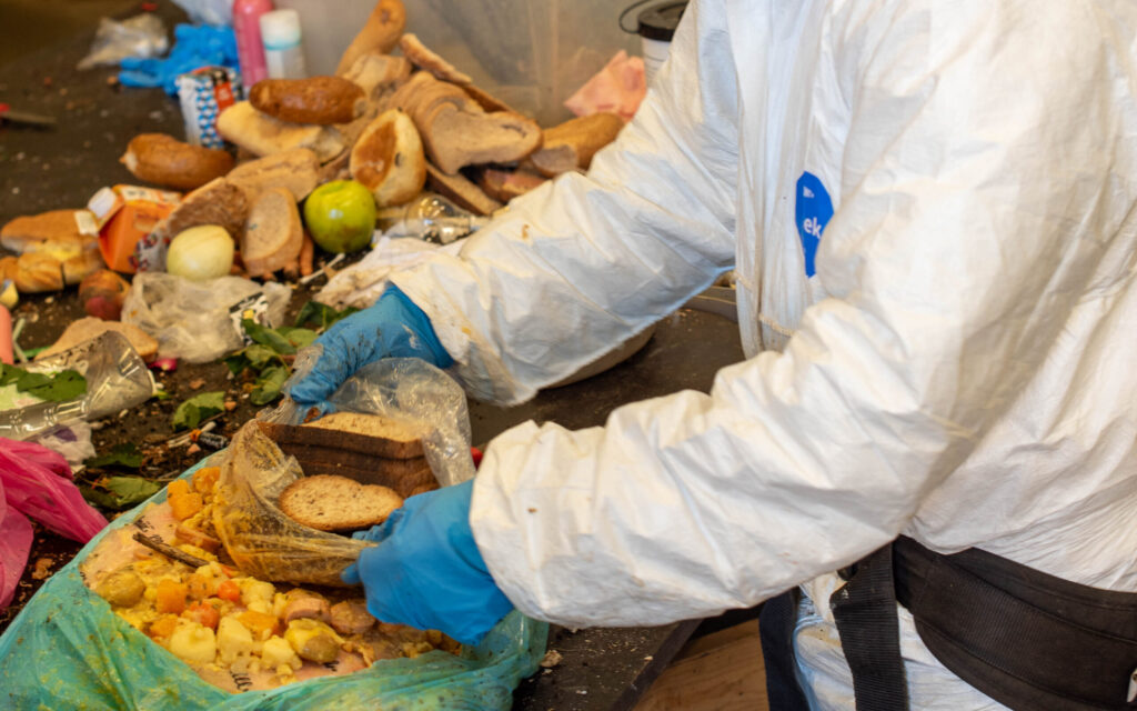 Medarbeider som åpner avfallspose med masse matavfall i forbindelse med sorteringsundersøkelse av restavfall.
