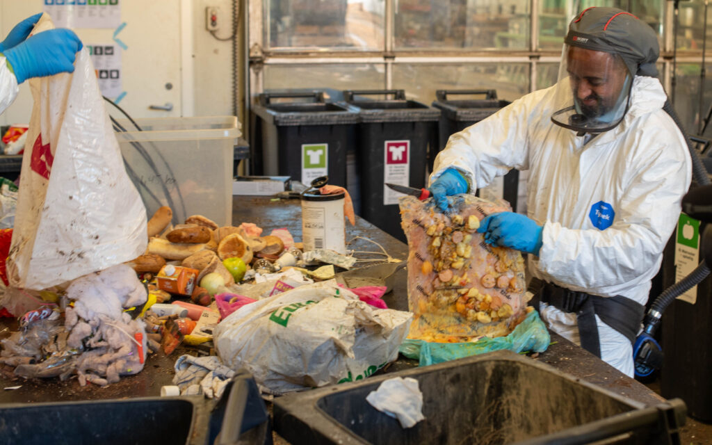 Medarbeider som åpner avfallspose med masse matavfall i forbindelse med sorteringsundersøkelse av restavfall.