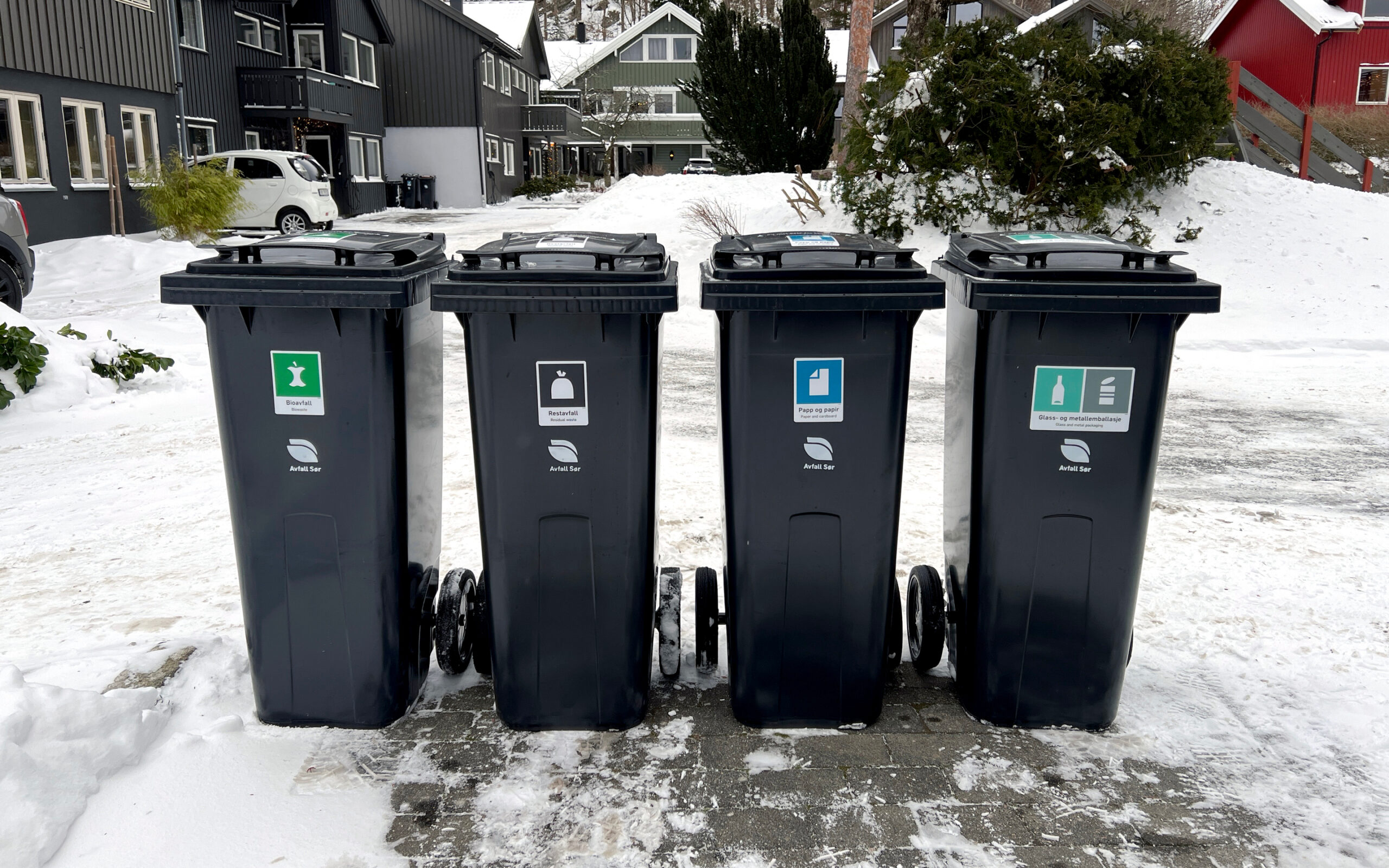 Avfallsdunker oppstilt på rekke mot vei utenfor bolig. Det er vinter. Dunkene er fri for snø og det er måket på oppstillingsplassen.