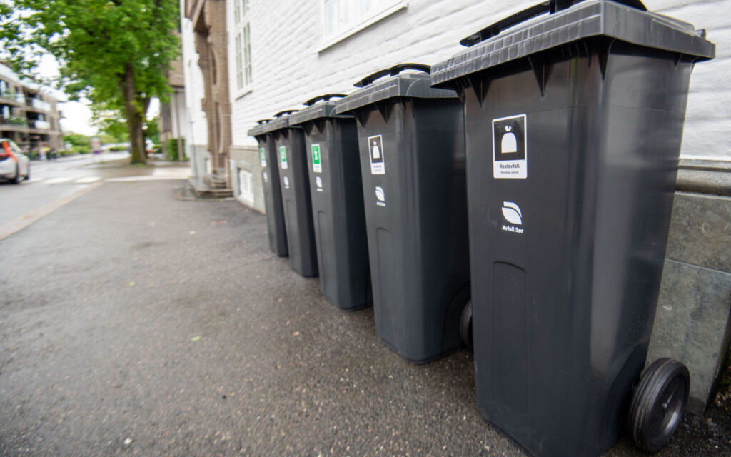 Avfallsdunker for restavfall og bioavfall på rekke utenfor bygg i sentrum.