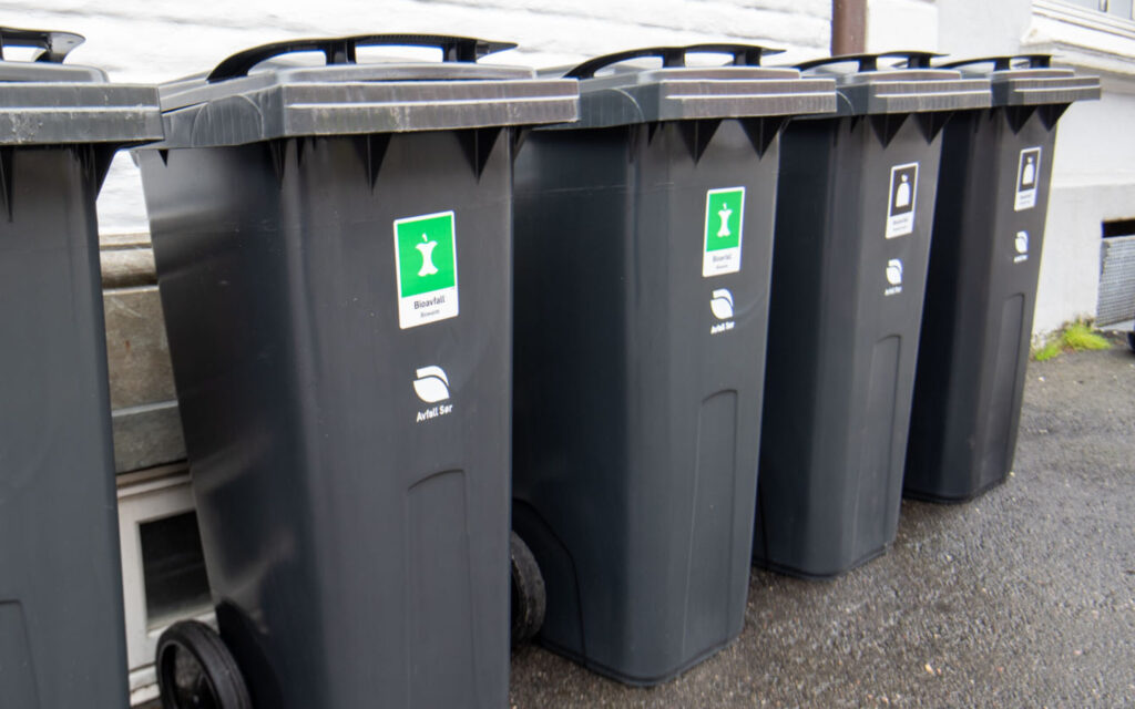 Avfallsdunker for restavfall og bioavfall på rekke utenfor bygg i sentrum.