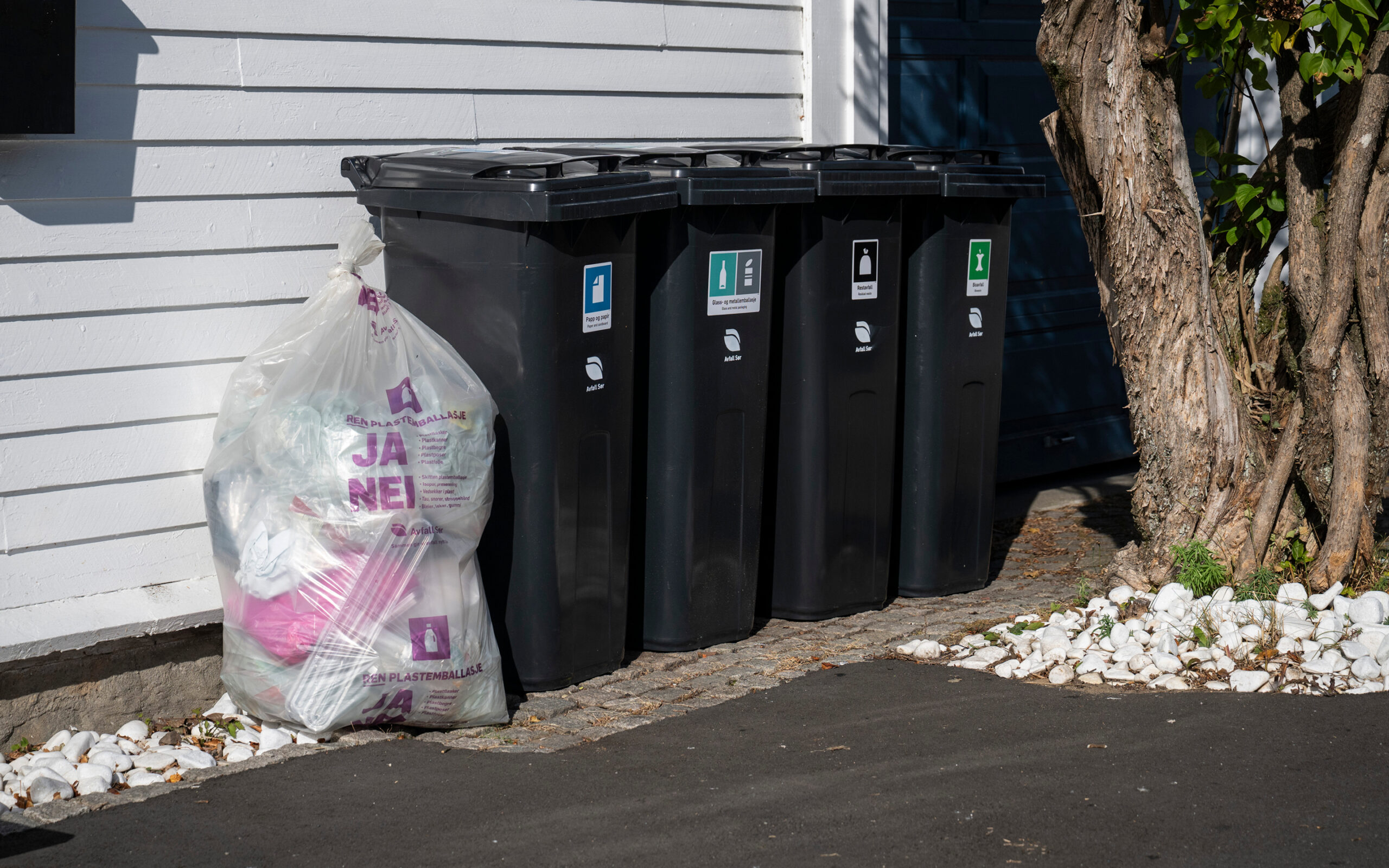Avfallsdunker og plastsekk oppstilt på rekke og rad l mot husvegg